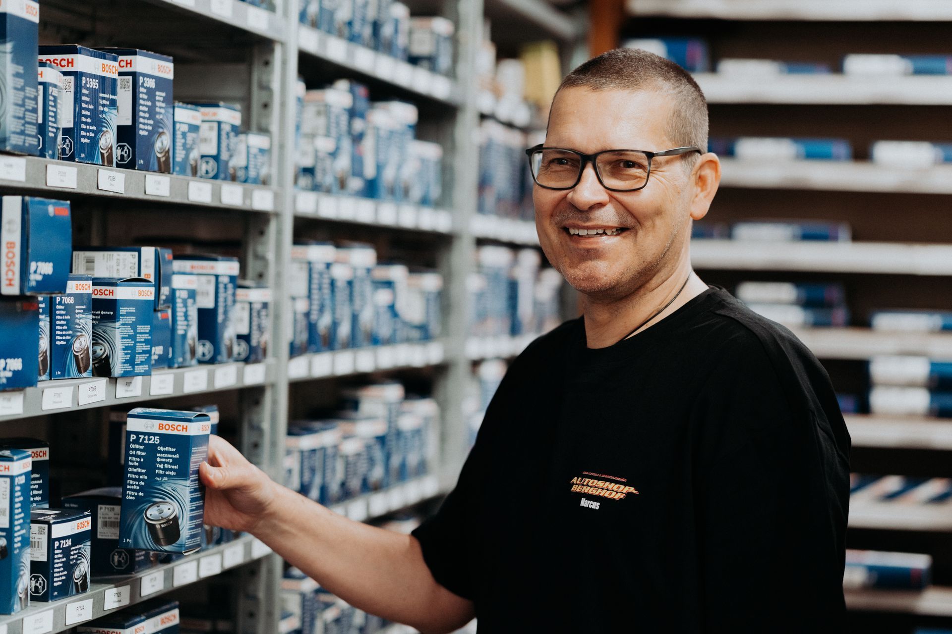 Ein Mann steht in einem Lager vor einem Regal mit Ersatzteilen.