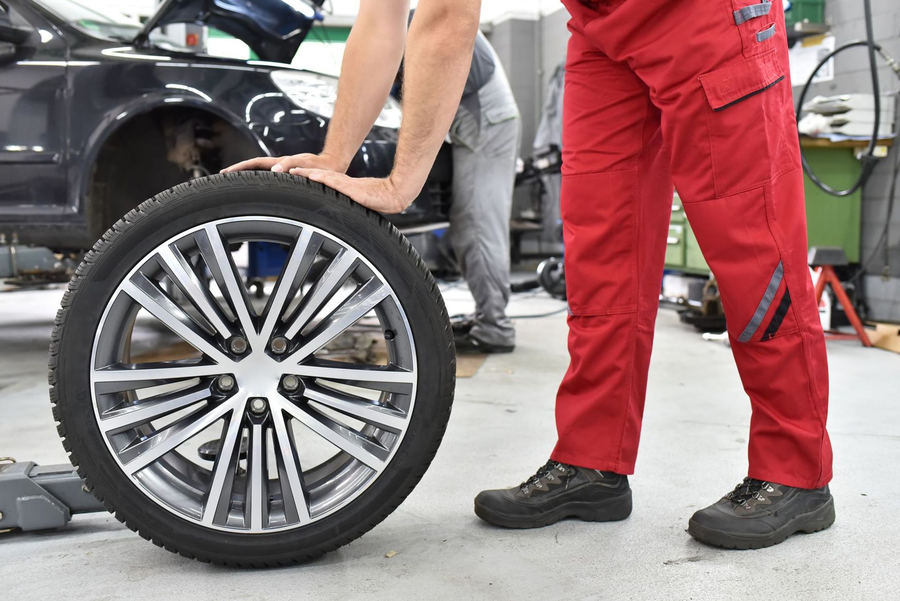 Un mécanicien tient un pneu de voiture dans un garage, avec un véhicule et des outils en arrière-plan.
