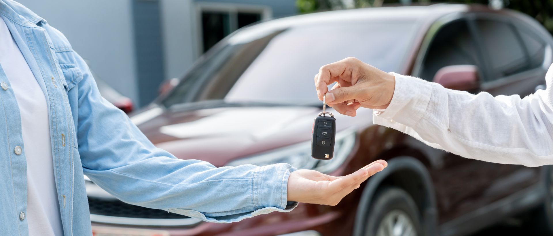 Remise des clés de voiture à côté d'un véhicule rouge chez un concessionnaire.