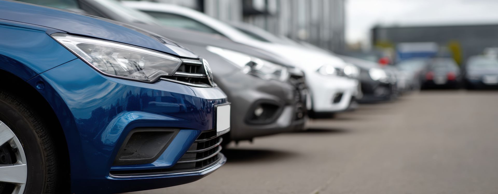 Rangée de voitures garées, avec une voiture bleue au premier plan sur le parking d'une concession automobile