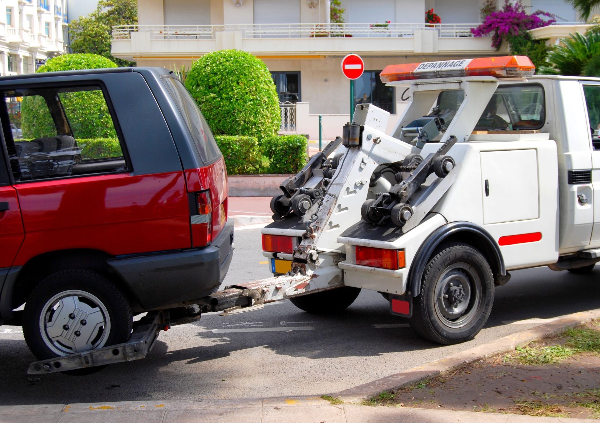Une dépanneuse soulève un SUV rouge dans une rue devant des maisons.