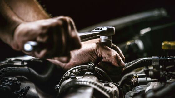 Un mécanicien serre une clé sur le moteur d'une voiture dans un garage faiblement éclairé.