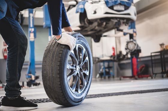 Un mécanicien fait rouler un pneu de voiture dans un atelier de réparation automobile.