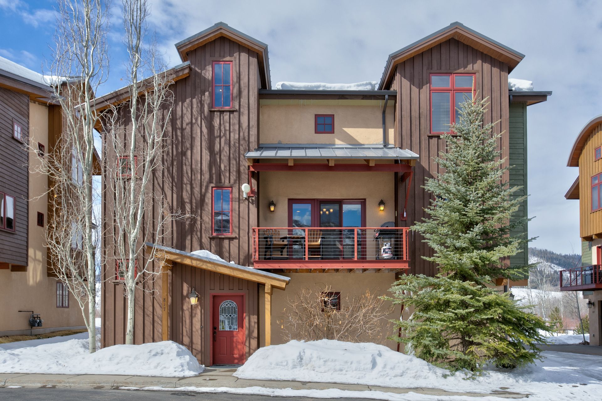 Townhouse with wood siding, balcony, and snow in a mountain setting.