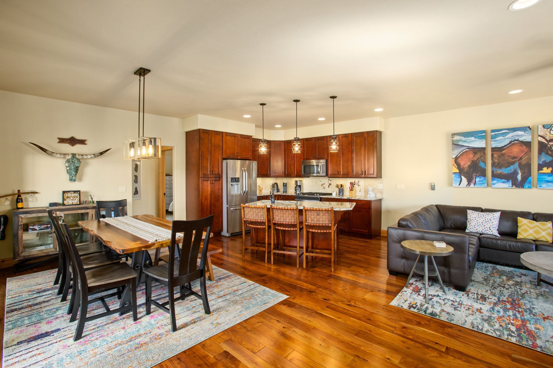 Open-concept living space with dining area, kitchen, and living room. Brown hardwood floors, wooden cabinets, and a rug.