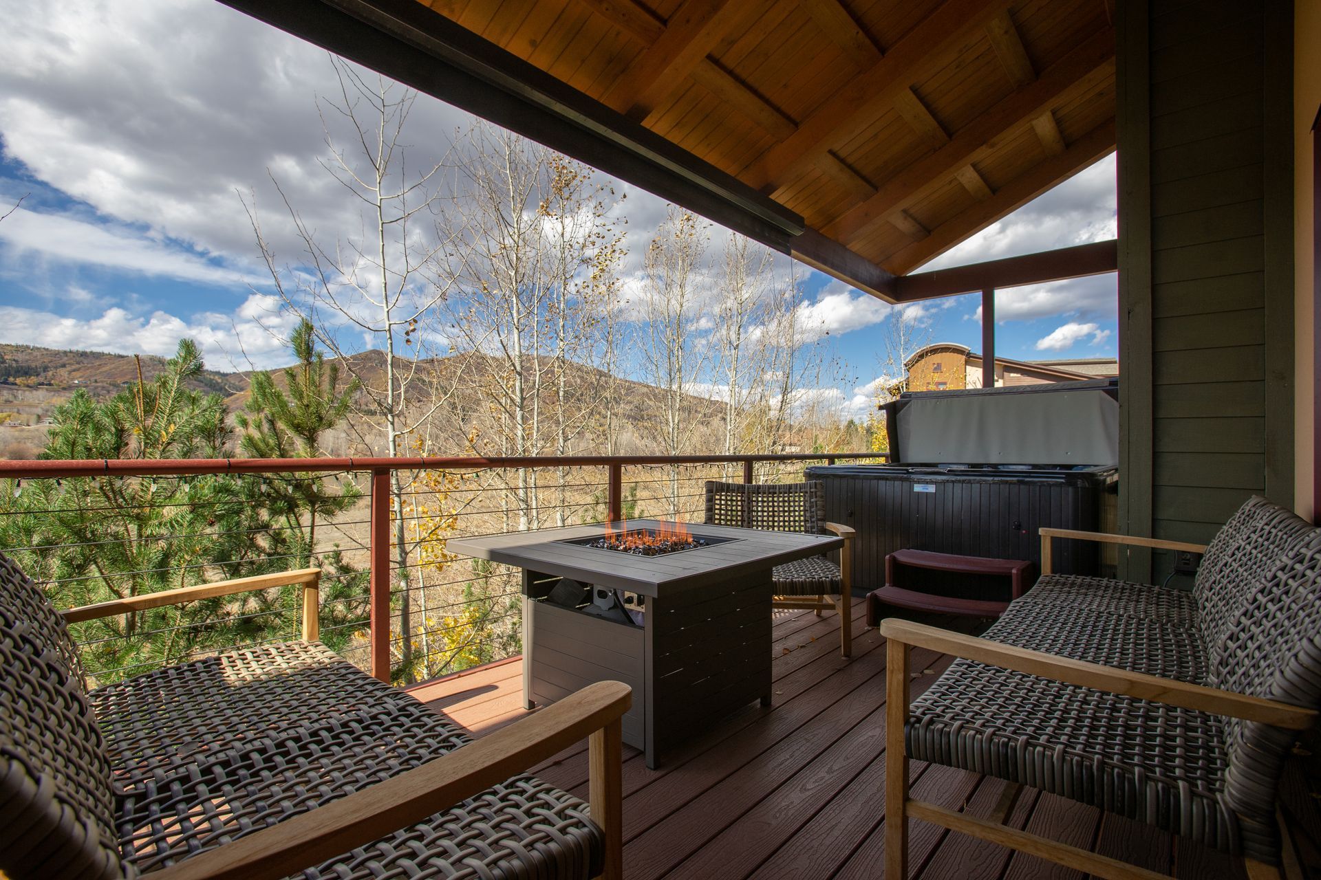 Deck with fire pit, hot tub, seating, and mountain views under a cloudy sky.