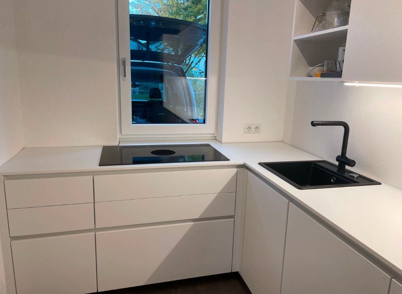 Eine Küche mit weißen Schränken, einem Ceranfeld und einem Spülbecken