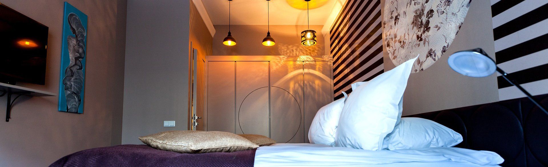 A bedroom with a bed , pillows , a television and a striped wall.