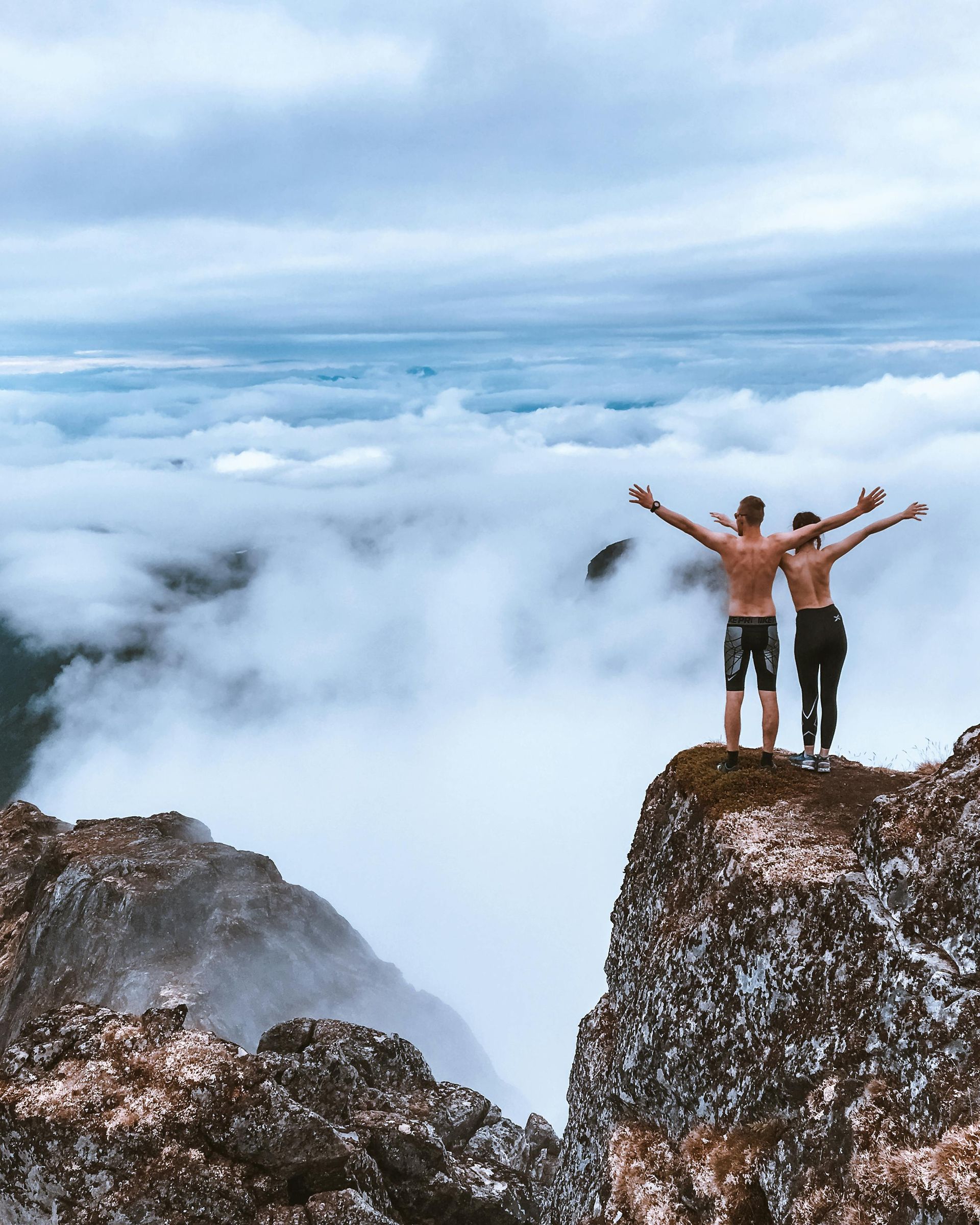 Two people are standing on top of a mountain with their arms outstretched.