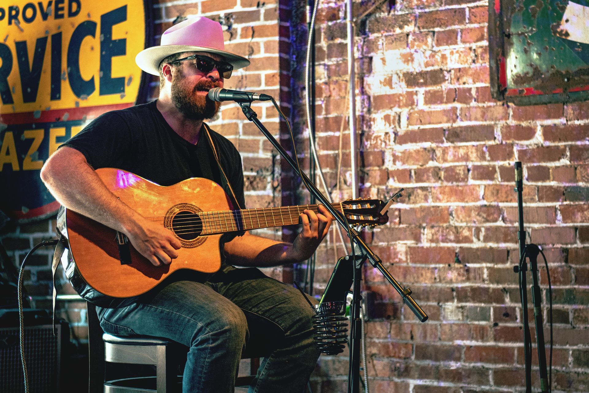 A man is singing into a microphone while playing a guitar in front of a brick wall.