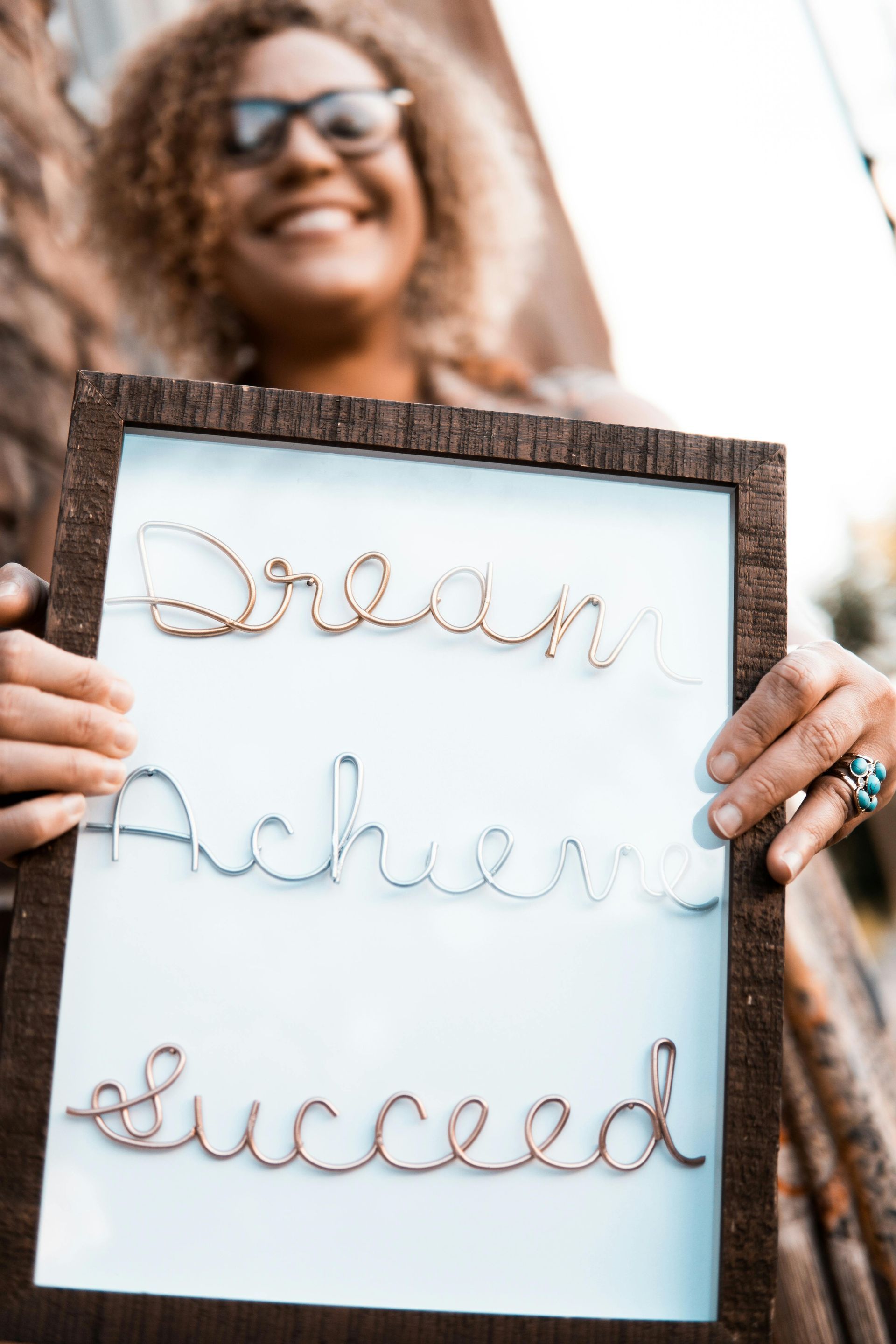 A woman is holding a sign that says `` dream achieve succeed ''.
