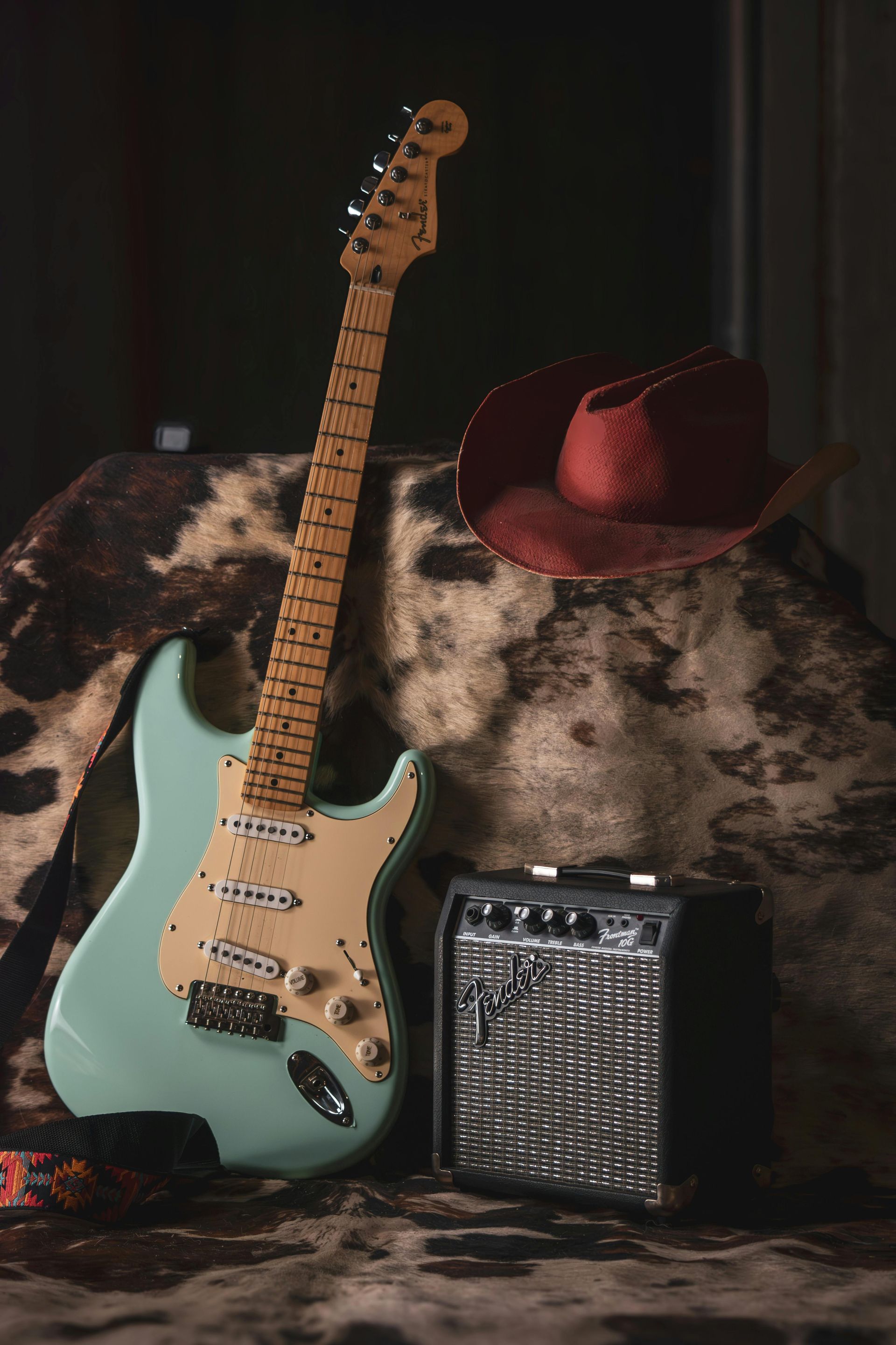 An electric guitar , amplifier , and cowboy hat are sitting on a rock.