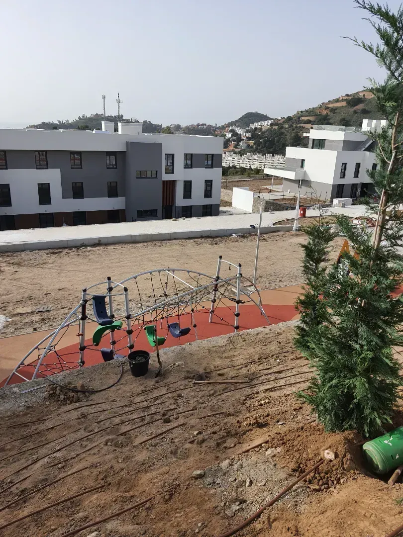 Se está construyendo un parque infantil en un campo de tierra frente a un edificio.