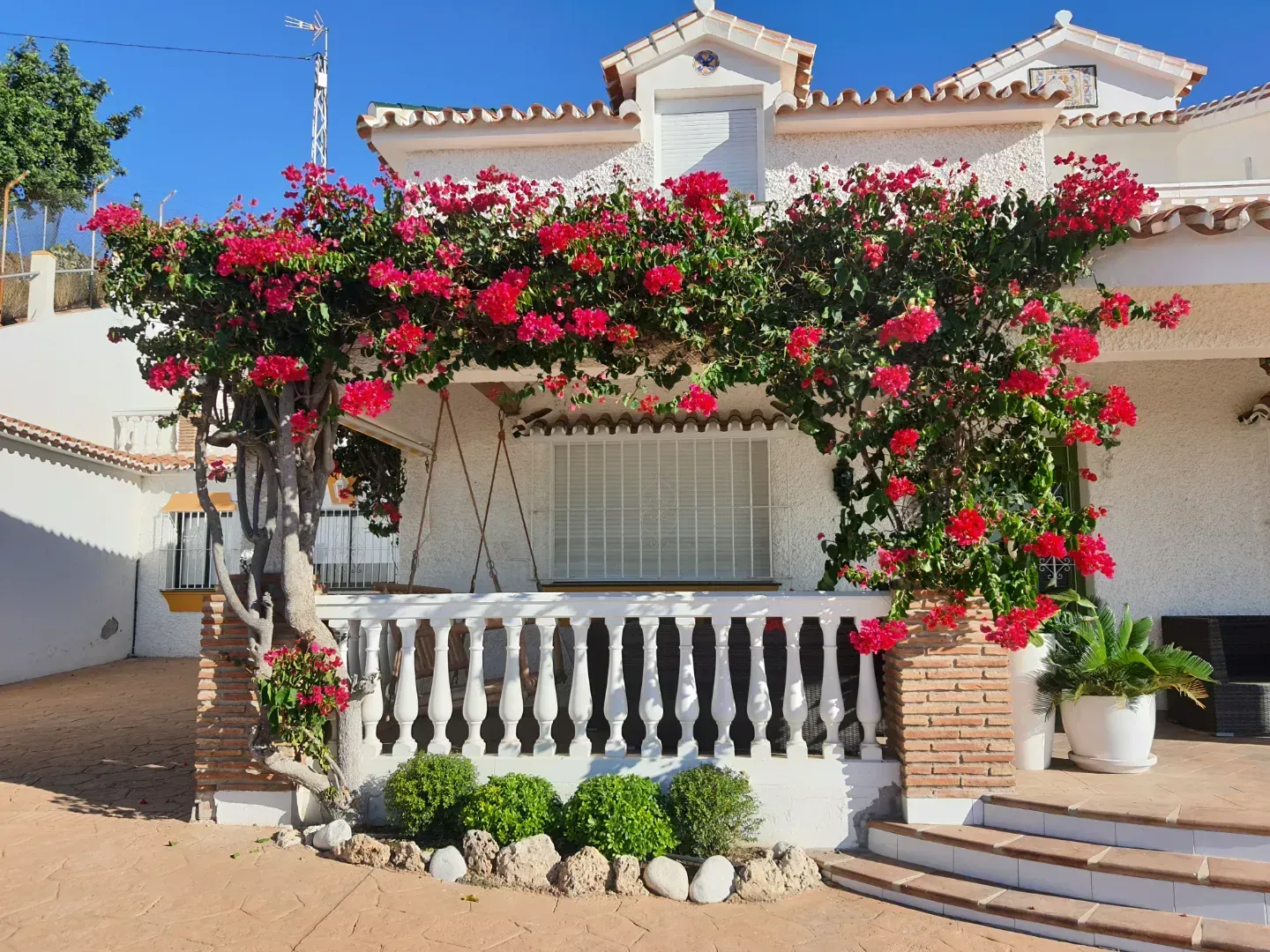 Una casa blanca con flores rojas en el porche