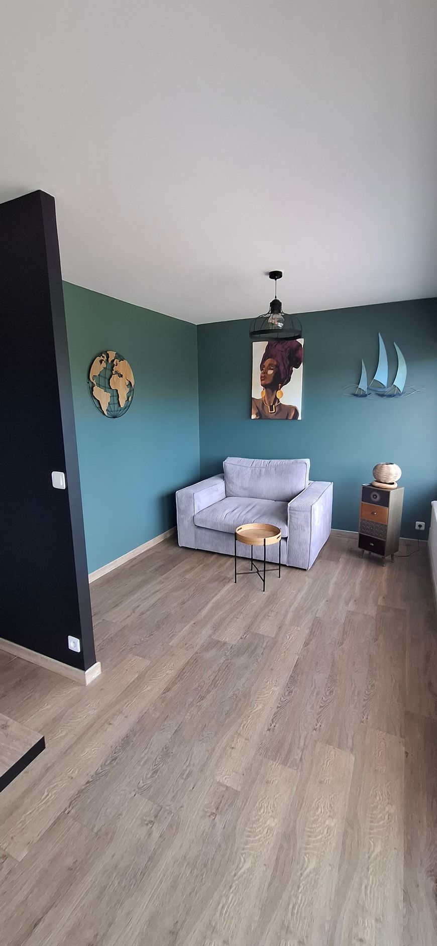 Salon moderne bleu sarcelle avec fauteuil gris, parquet, tableaux et décoration sur le thème nautique