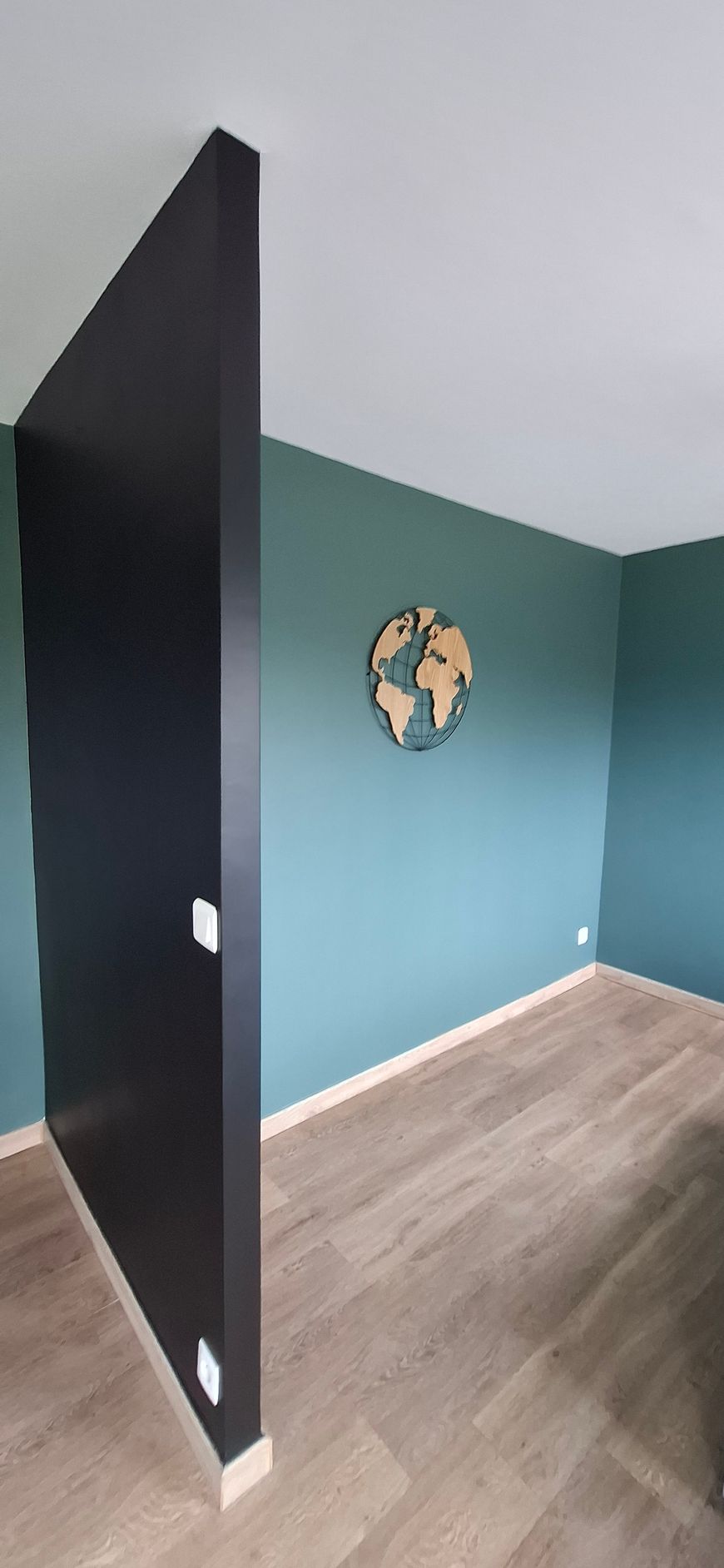 Vue d'angle d'une pièce aux murs turquoise, au parquet clair et ornée d'une carte du monde en bois sur le mur du fond.