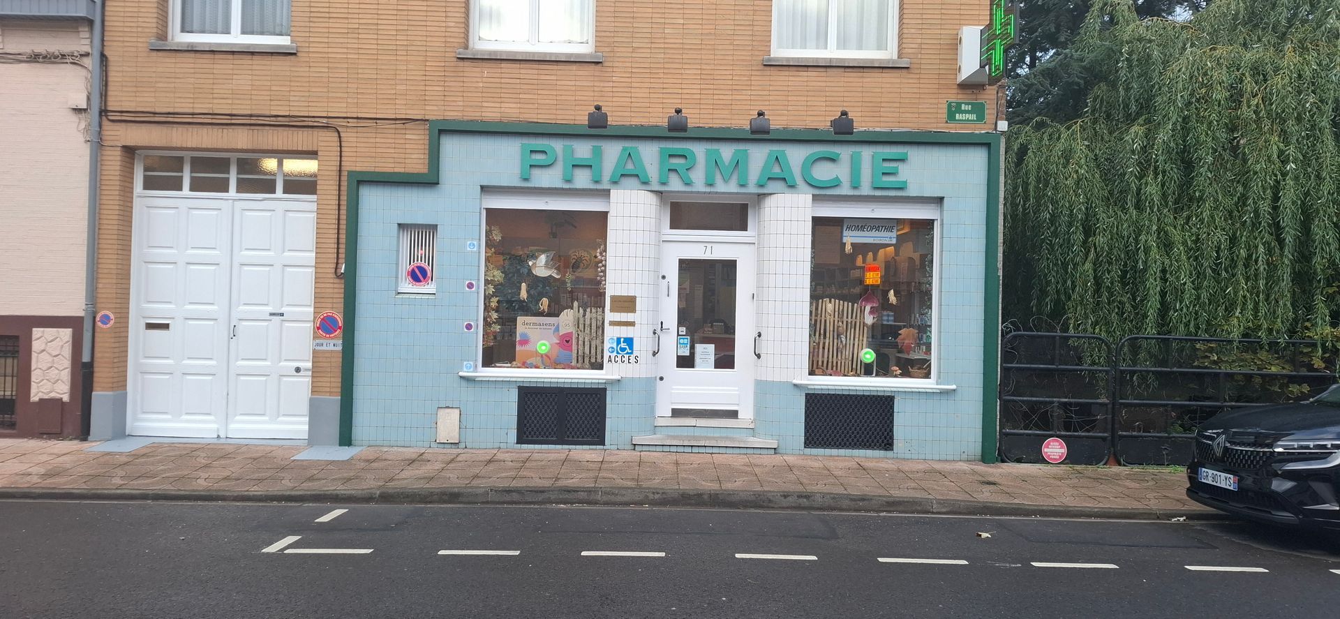 Une façade de pharmacie bleu clair avec de grandes vitrines, une porte centrale et une enseigne PHARMACIE  au-dessus.