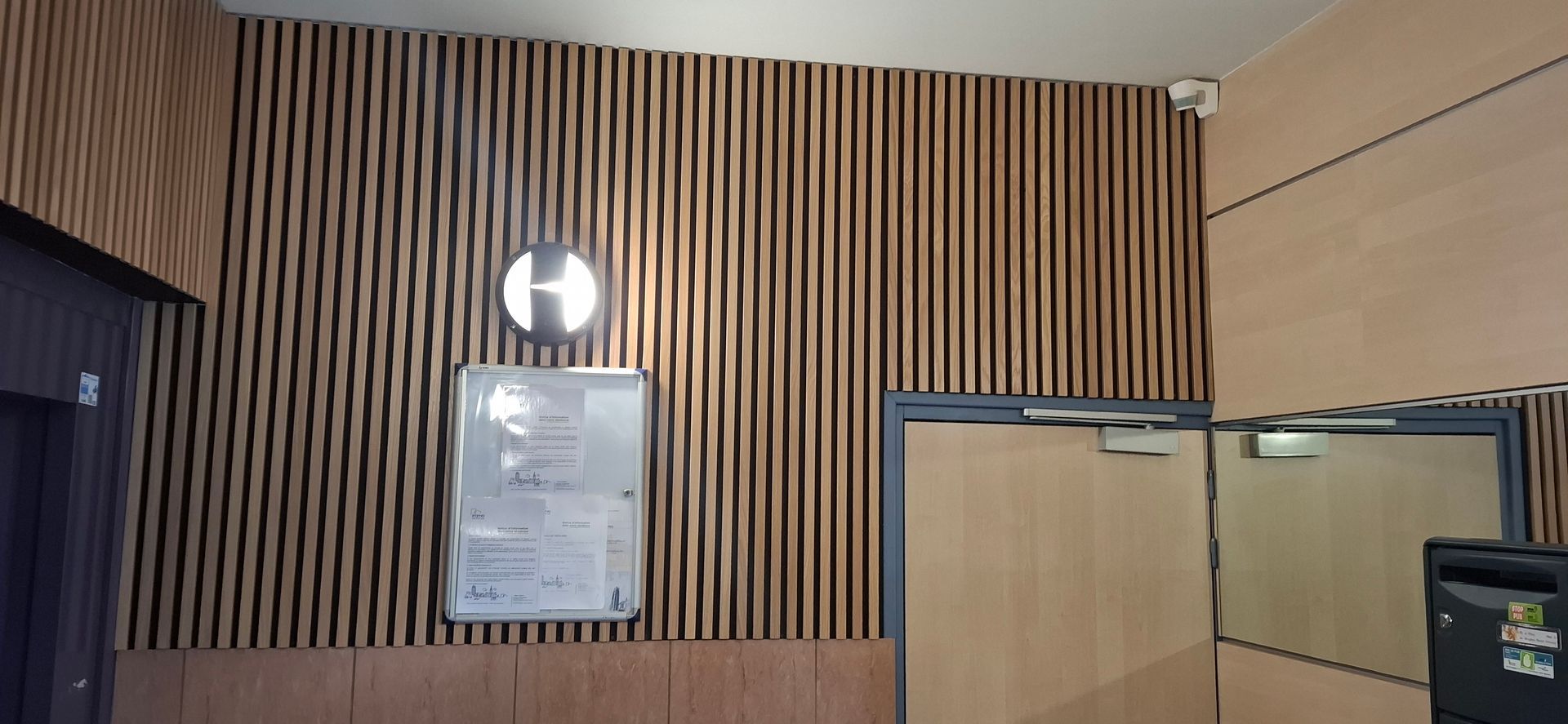 Mur du hall d'entrée avec des lattes de bois verticales, une enseigne et une porte vitrée.