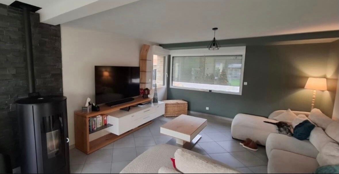 Un salon moderne avec une cheminée en pierre, une grande télévision sur une console blanche, une table basse et un canapé d'angle blanc.