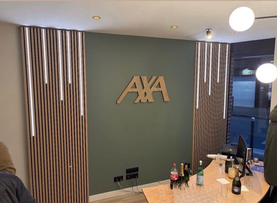 Logo AXA sur un mur vert encadré de panneaux de bois décoratifs avec éclairage vertical dans un espace de bureaux moderne.
