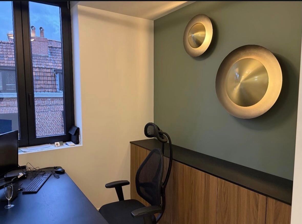 Un bureau avec un ordinateur, une chaise de bureau et des armoires sont adossés à un mur vert orné de deux décorations murales métalliques circulaires.