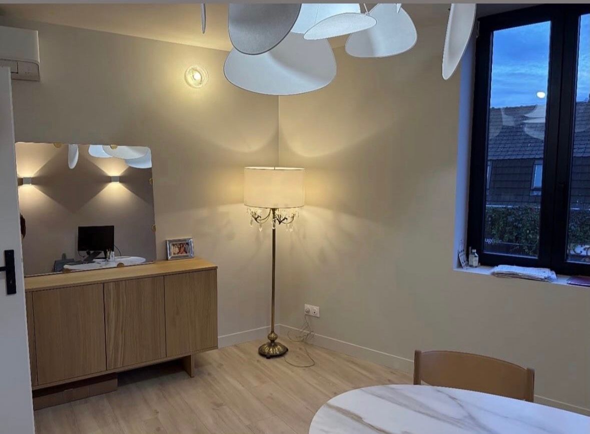 Une salle à manger lumineuse avec un buffet en bois, un lampadaire, une table en marbre et un grand plafonnier en forme de pétales.