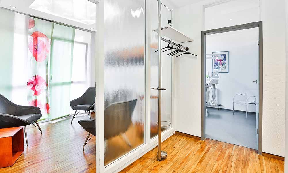 Ein Wartezimmer mit Stühlen, Garderobe und Glaswand.