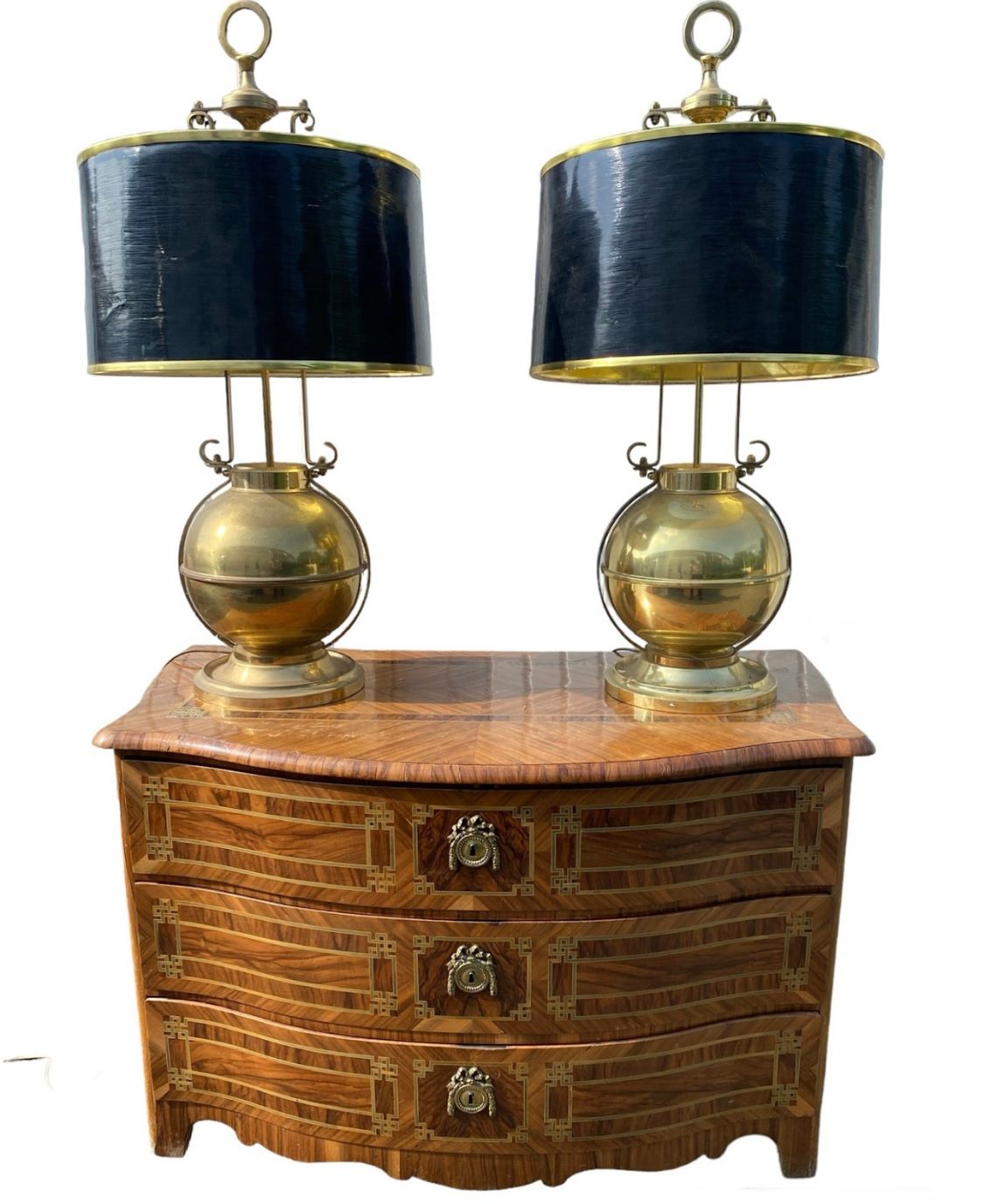 Un coffre en bois à trois tiroirs, surmonté de deux lampes en laiton à abat-jour noirs.