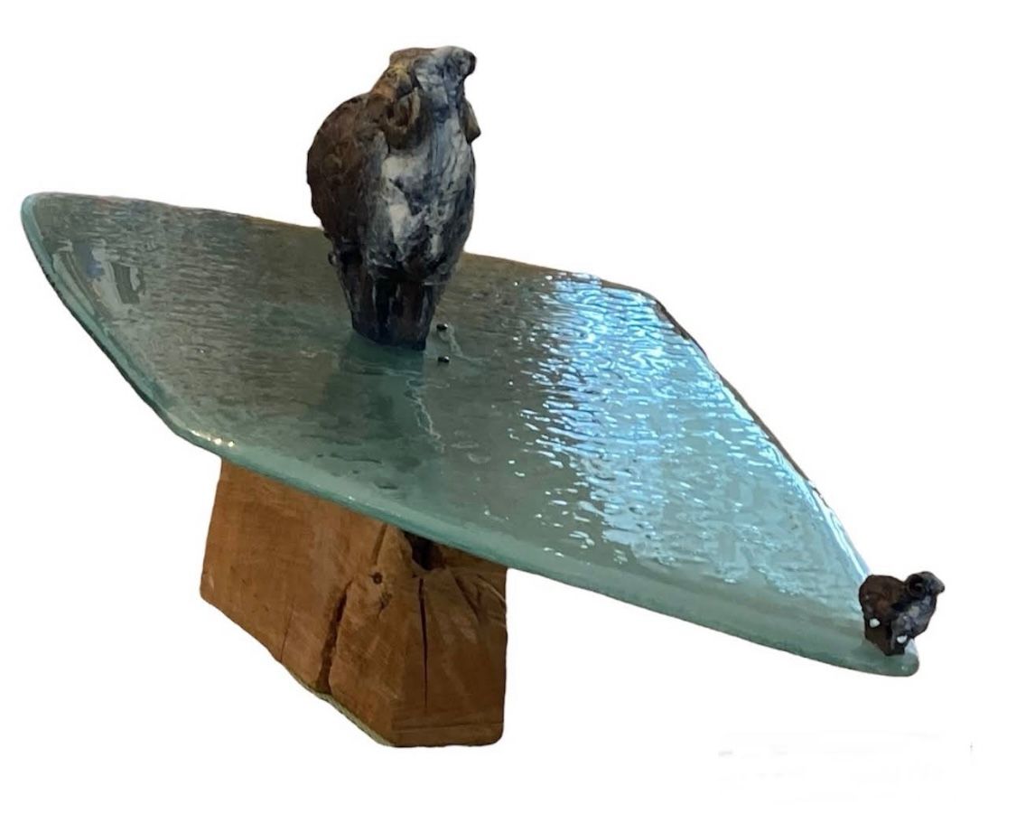 Une sculpture de hibou en céramique repose en équilibre sur une plaque de verre soutenue par un bloc de bois.