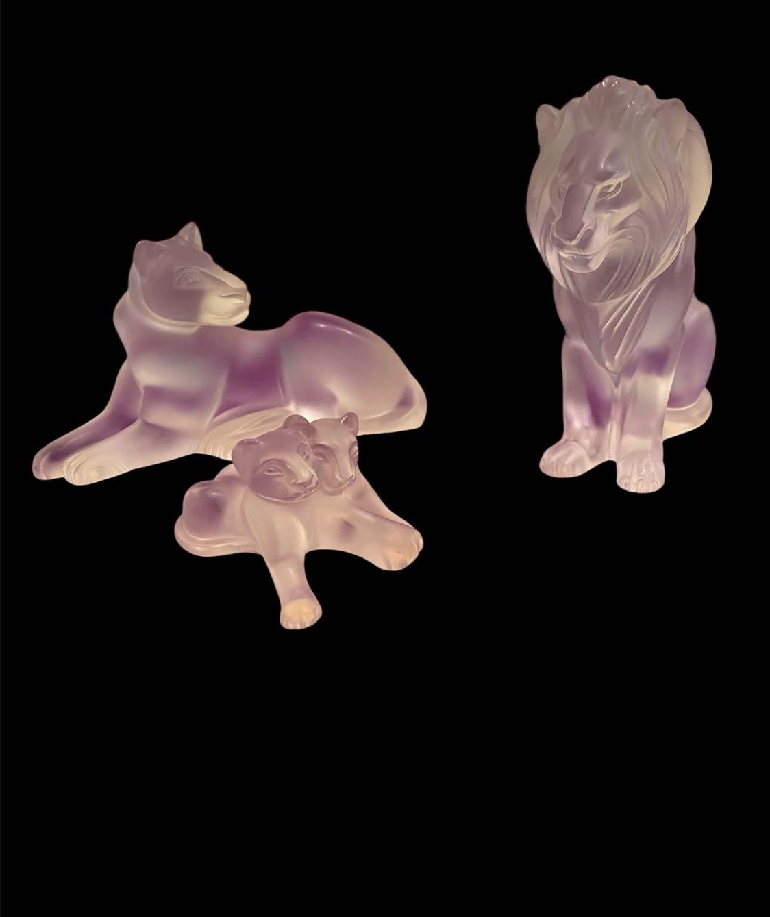 Trois figurines de lions en améthyste translucide sculptée sur fond noir.