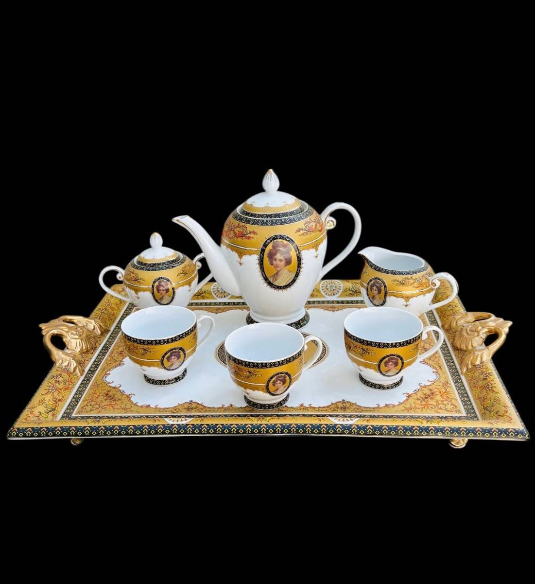 Service à thé doré et blanc sur un plateau décoré avec tasses, théière, pot à lait et sucrier.