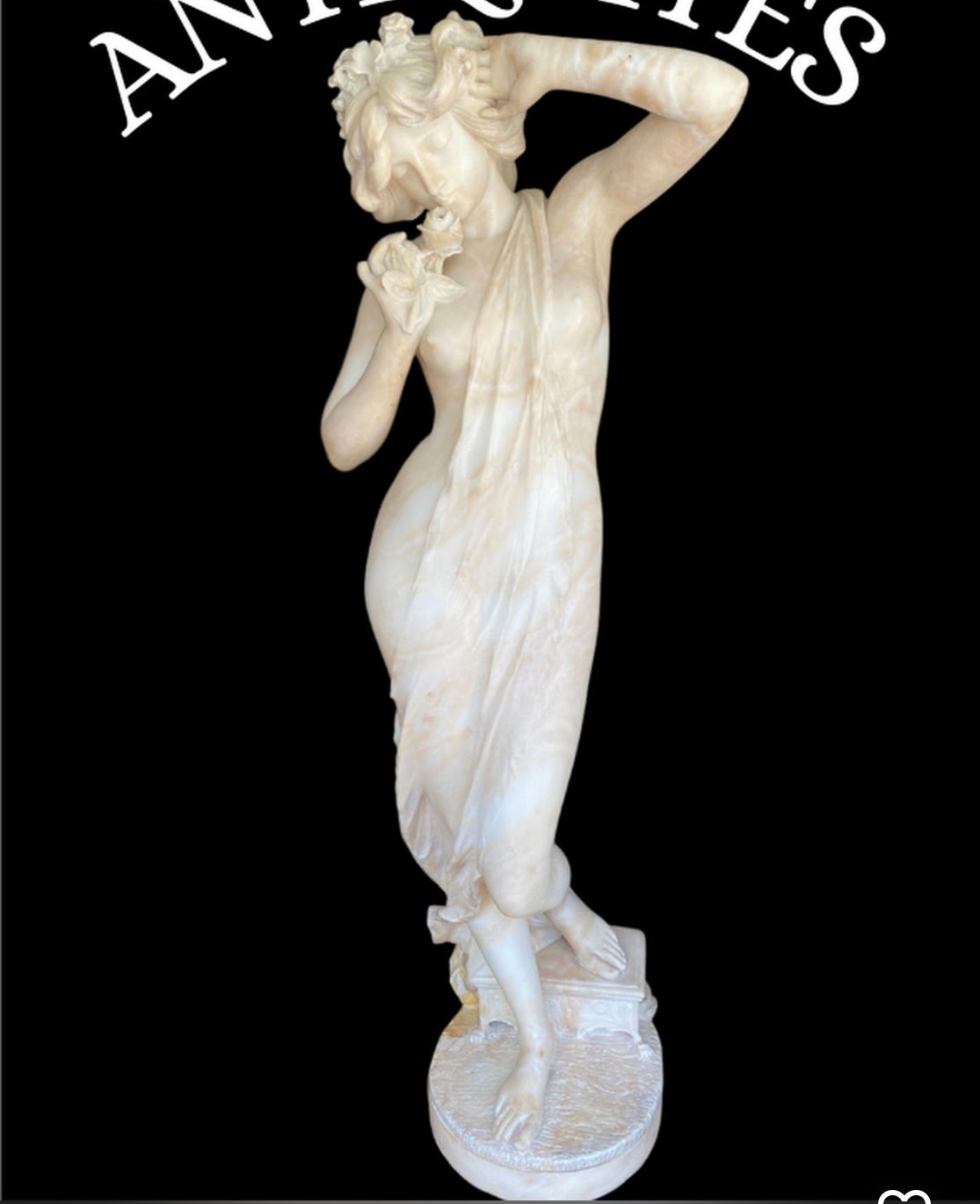 Statue en marbre d'une femme drapée de draperies fluides, les bras levés, sur un socle rond.