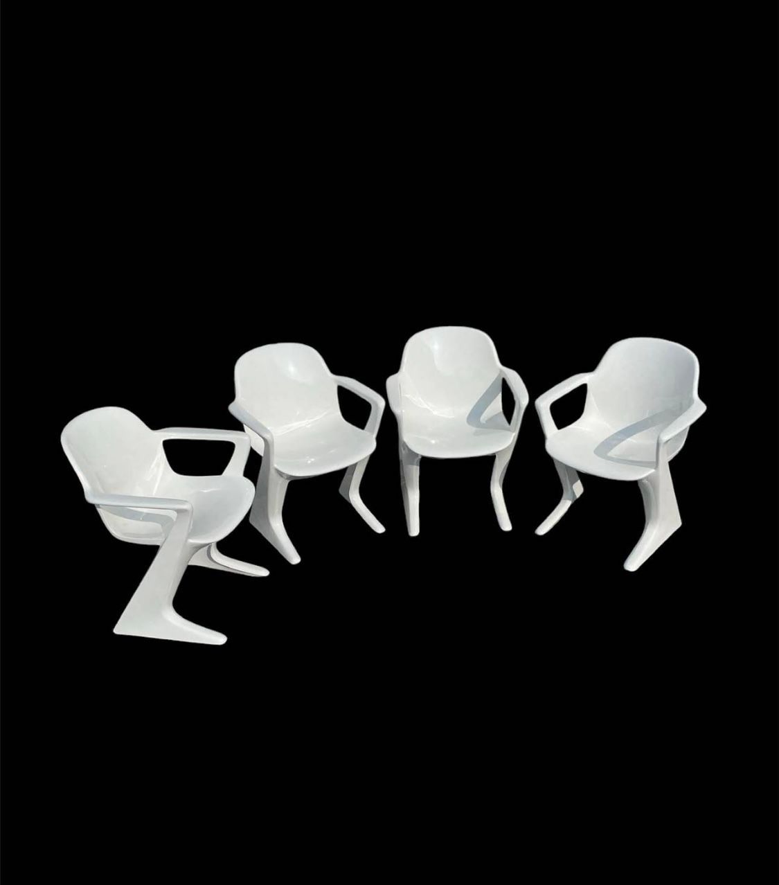 Quatre chaises en plastique blanc sur fond noir.