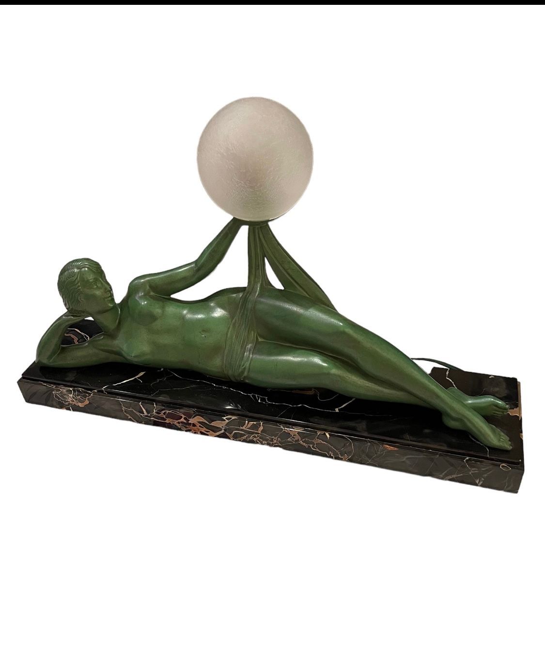 Figurine verte allongée tenant une sphère blanche, sur un socle rectangulaire sombre.