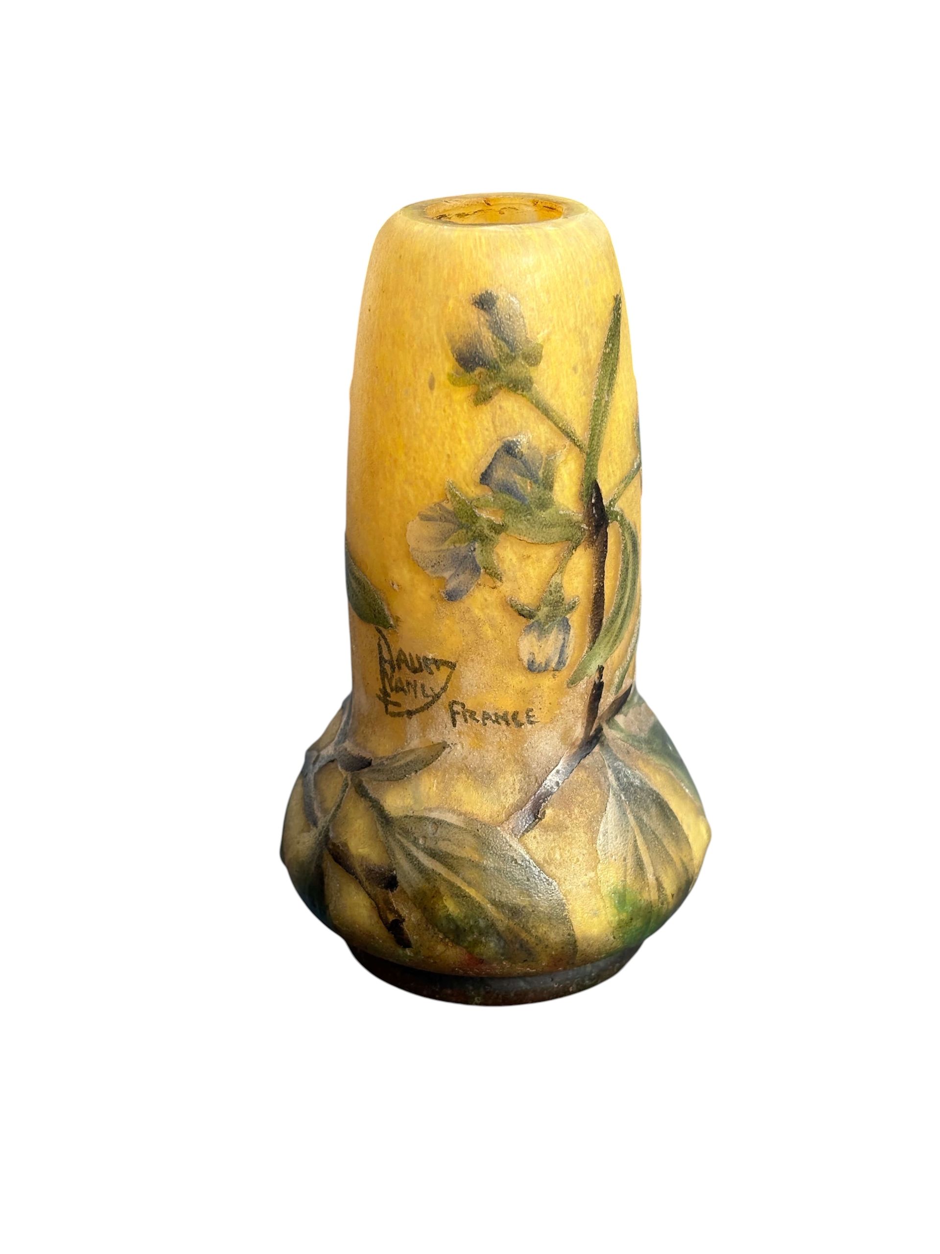 Petit vase Daum jaune orné d'une peinture florale et de feuilles vertes.