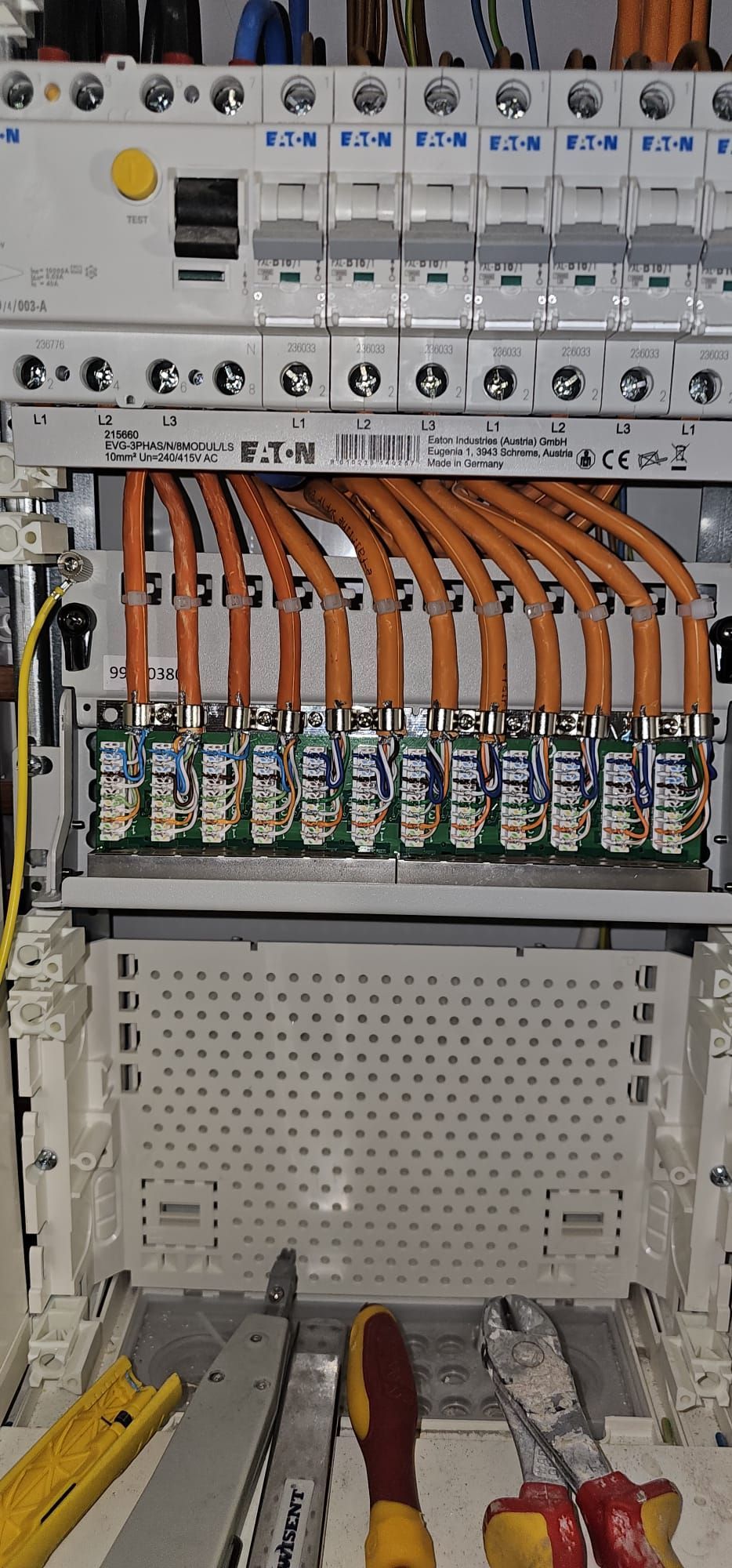 Ein Elektriker, der mit Handschuhen an elektrischen Bauteilen in einem Schaltschrank mit einem Multimeter arbeitet.
