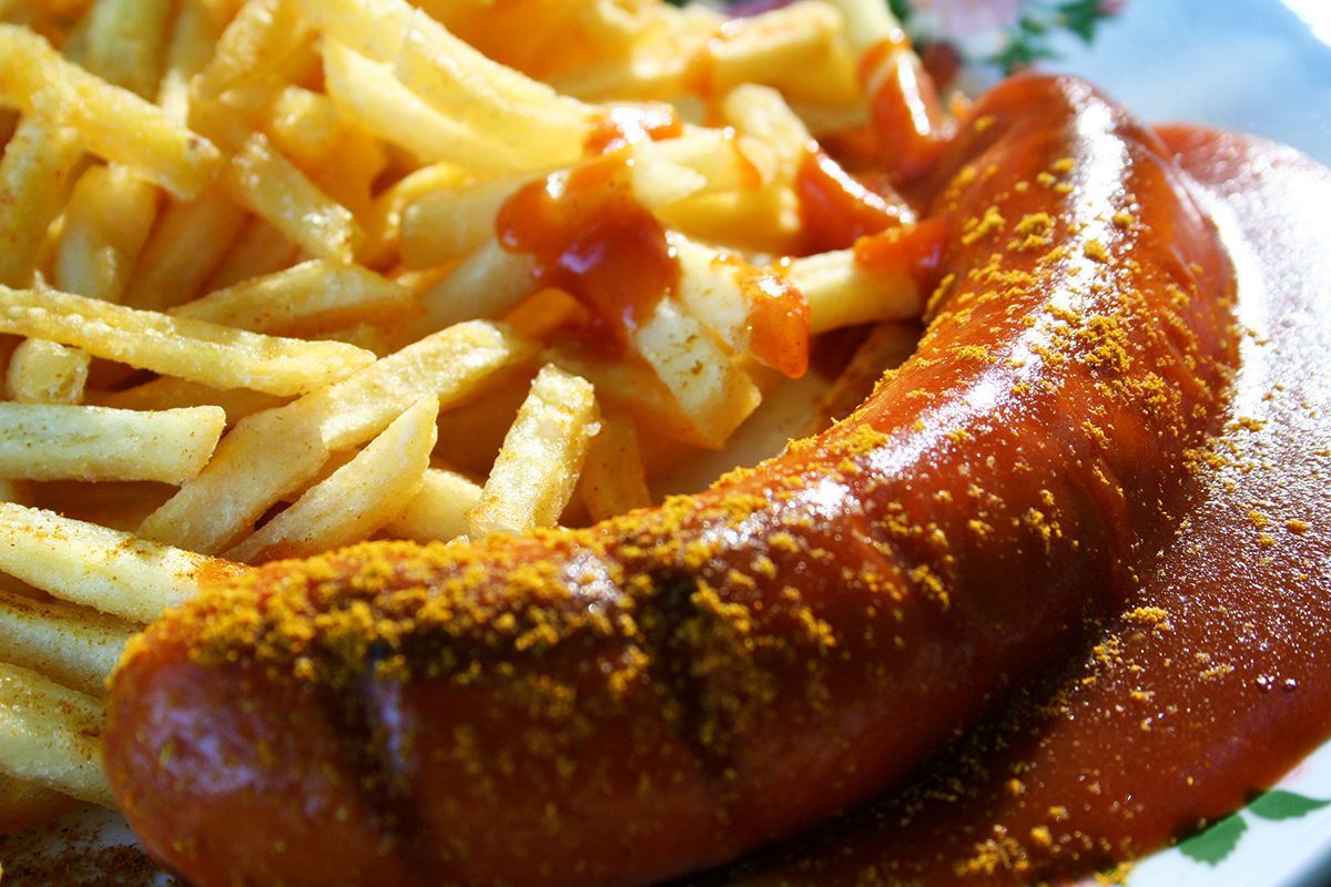 Ein Teller mit Pommes Frites und einer Wurst mit Currypulver darauf