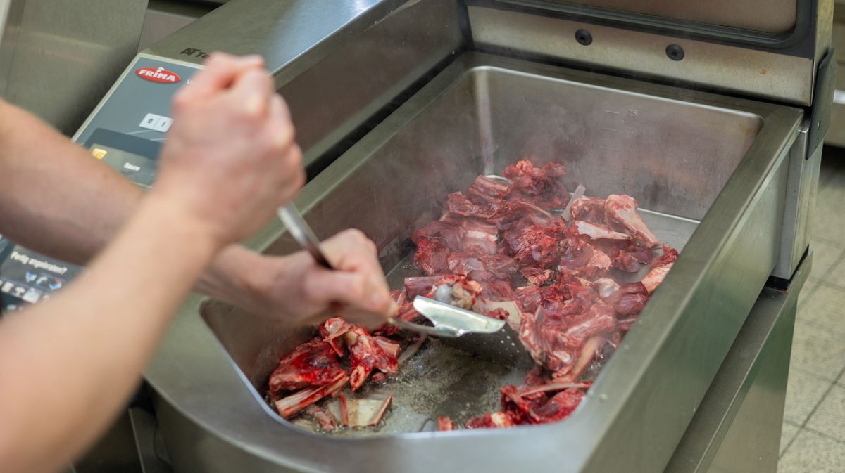 Eine Person bereitet mit einem Spatel Fleisch in einer Fritteuse zu.