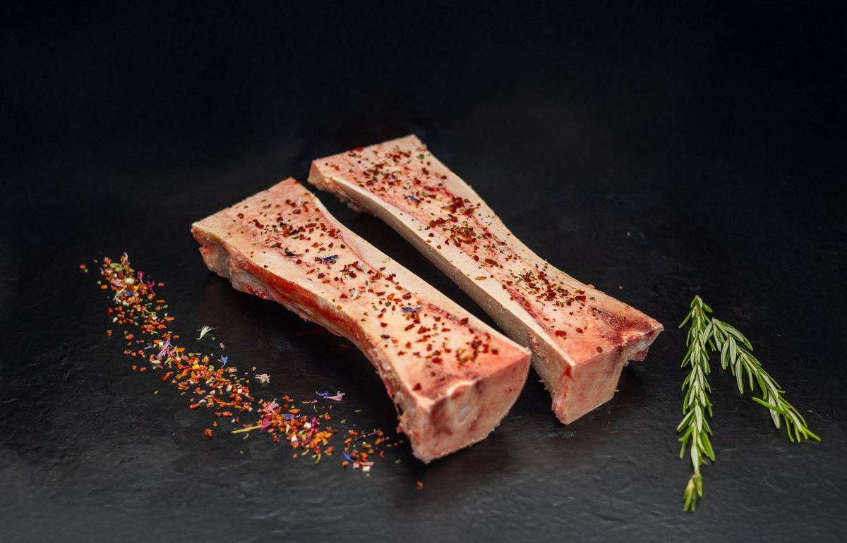 Zwei rohe Knochen mit Gewürzen auf einer schwarzen Oberfläche.
