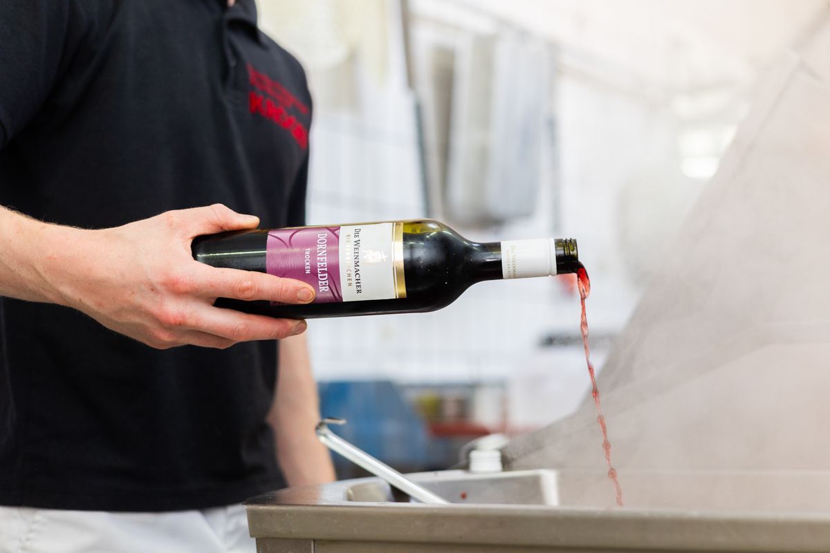 Ein Mann gießt eine Flasche Wein in einen Behälter.