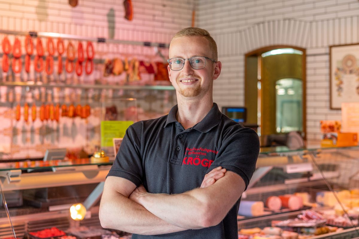 Ein Mann steht mit verschränkten Armen in einer Metzgerei.