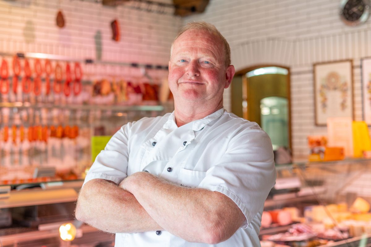 Ein Mann steht mit verschränkten Armen in einer Metzgerei.