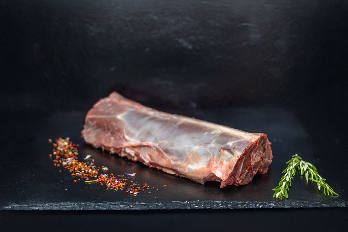 Ein Stück rohes Fleisch liegt auf einem schwarzen Schneidebrett.