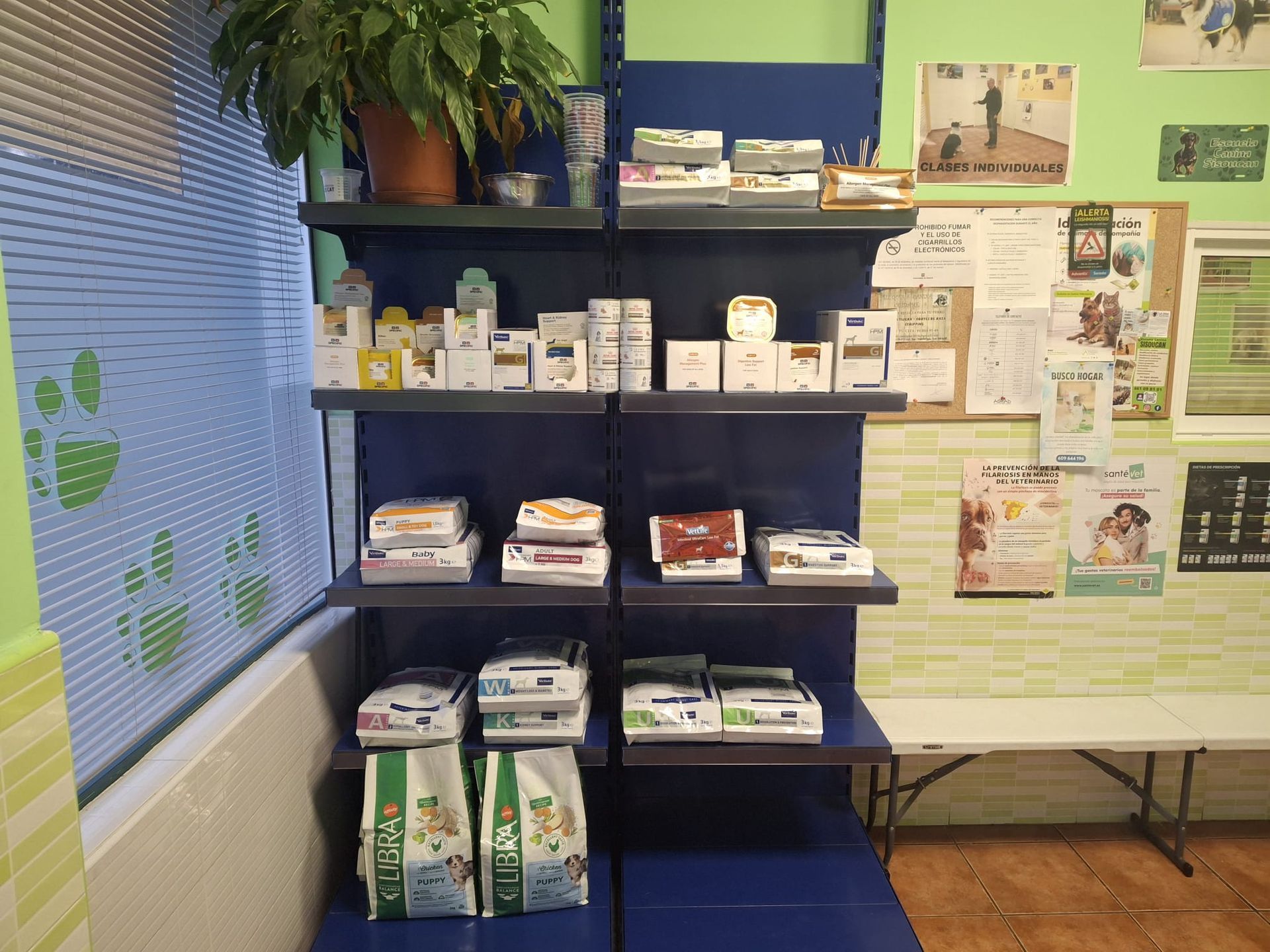 Estantes llenos de medicamentos y alimentos para mascotas en una clínica veterinaria, cerca de una ventana y una sala de espera.
