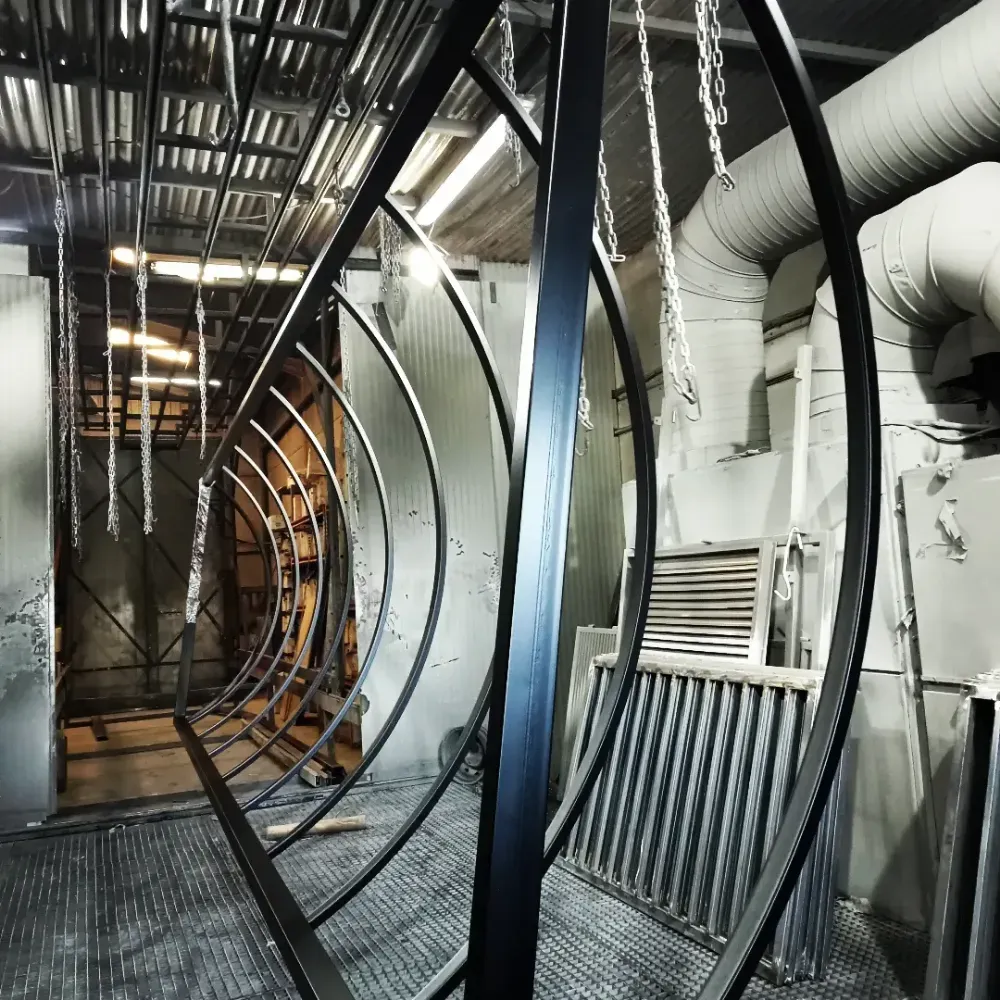 Pasillo industrial con paredes curvas de malla metálica, tuberías y conductos aéreos en un interior que recuerda a una fábrica.
