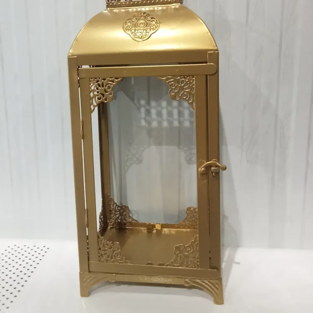Farol decorativo dorado con paneles de vidrio sobre una superficie blanca.