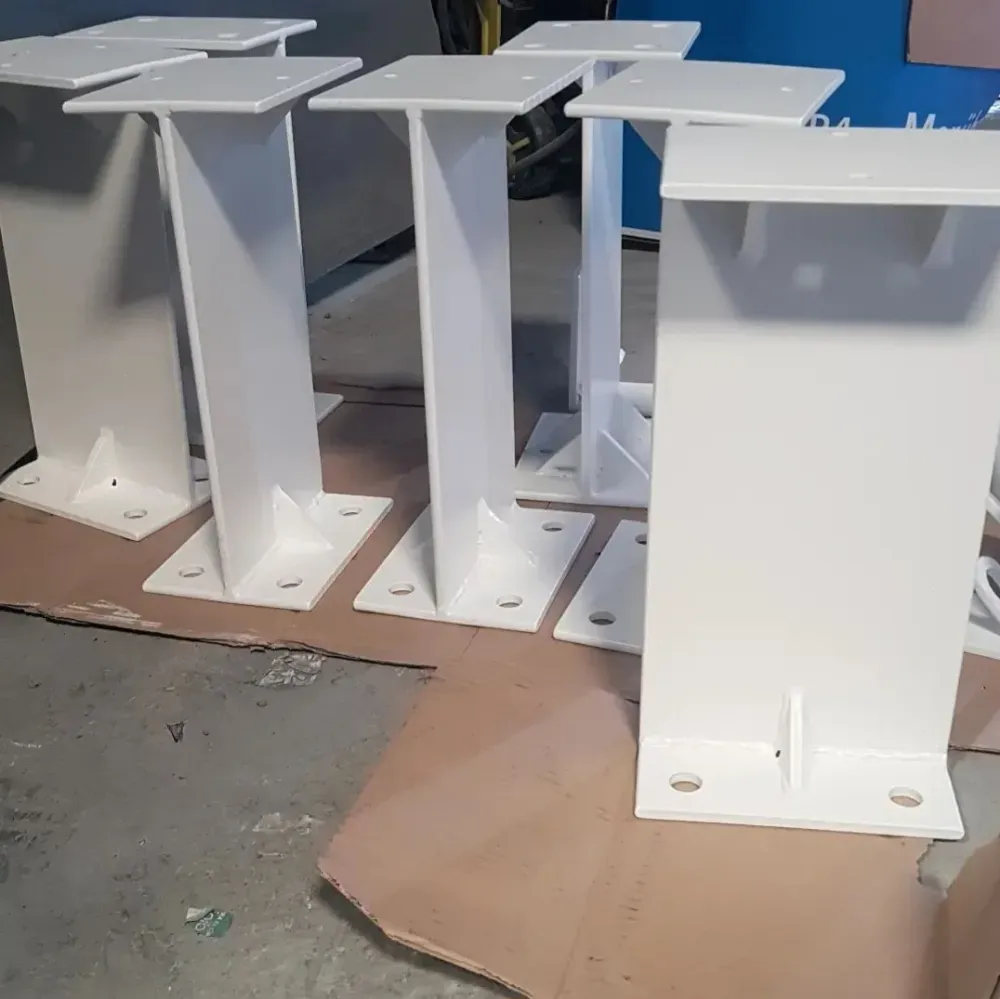 Bases de pedestal de metal blanco apiladas sobre cartón en un taller o área de almacenamiento.