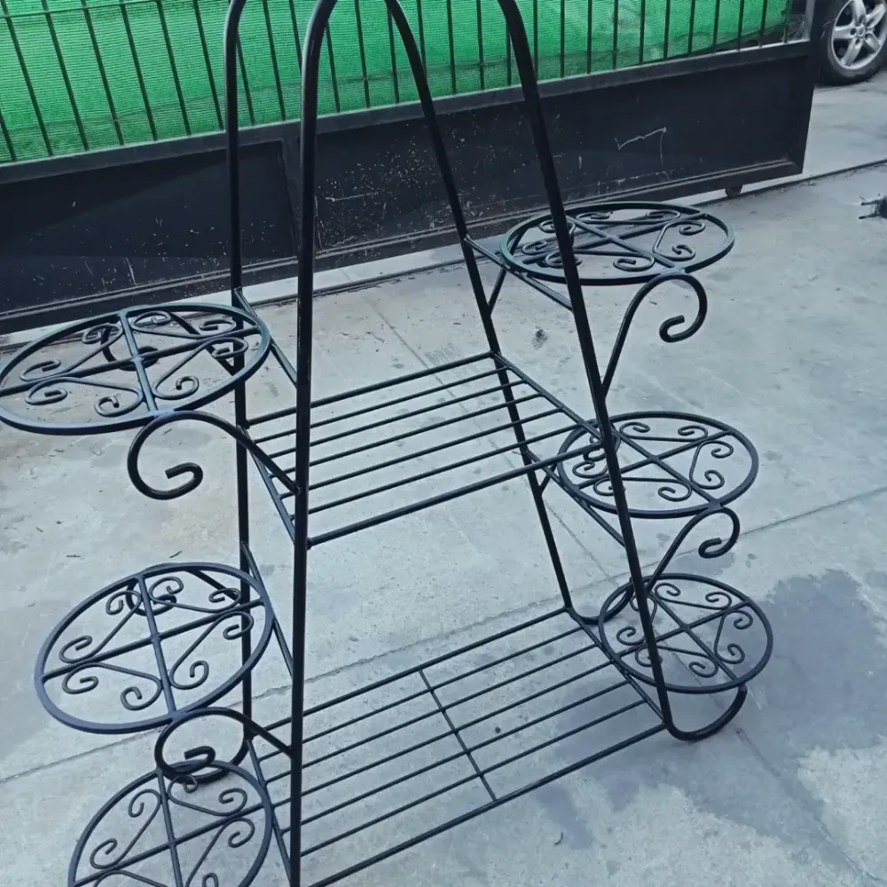 Soporte para plantas de hierro forjado negro con cuatro estantes circulares sobre un patio de hormigón.
