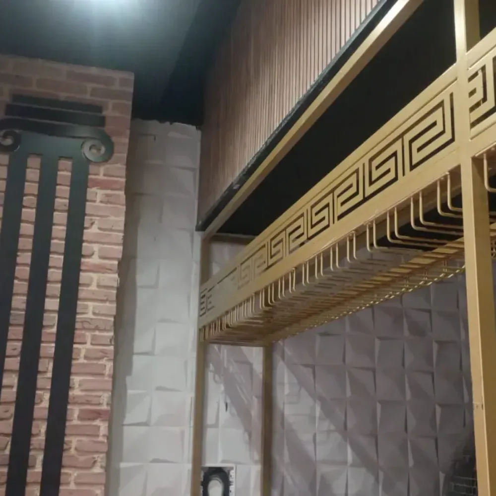 Estantería decorativa dorada junto a una pared de ladrillo visto y azulejos estampados en un espacio interior estrecho.