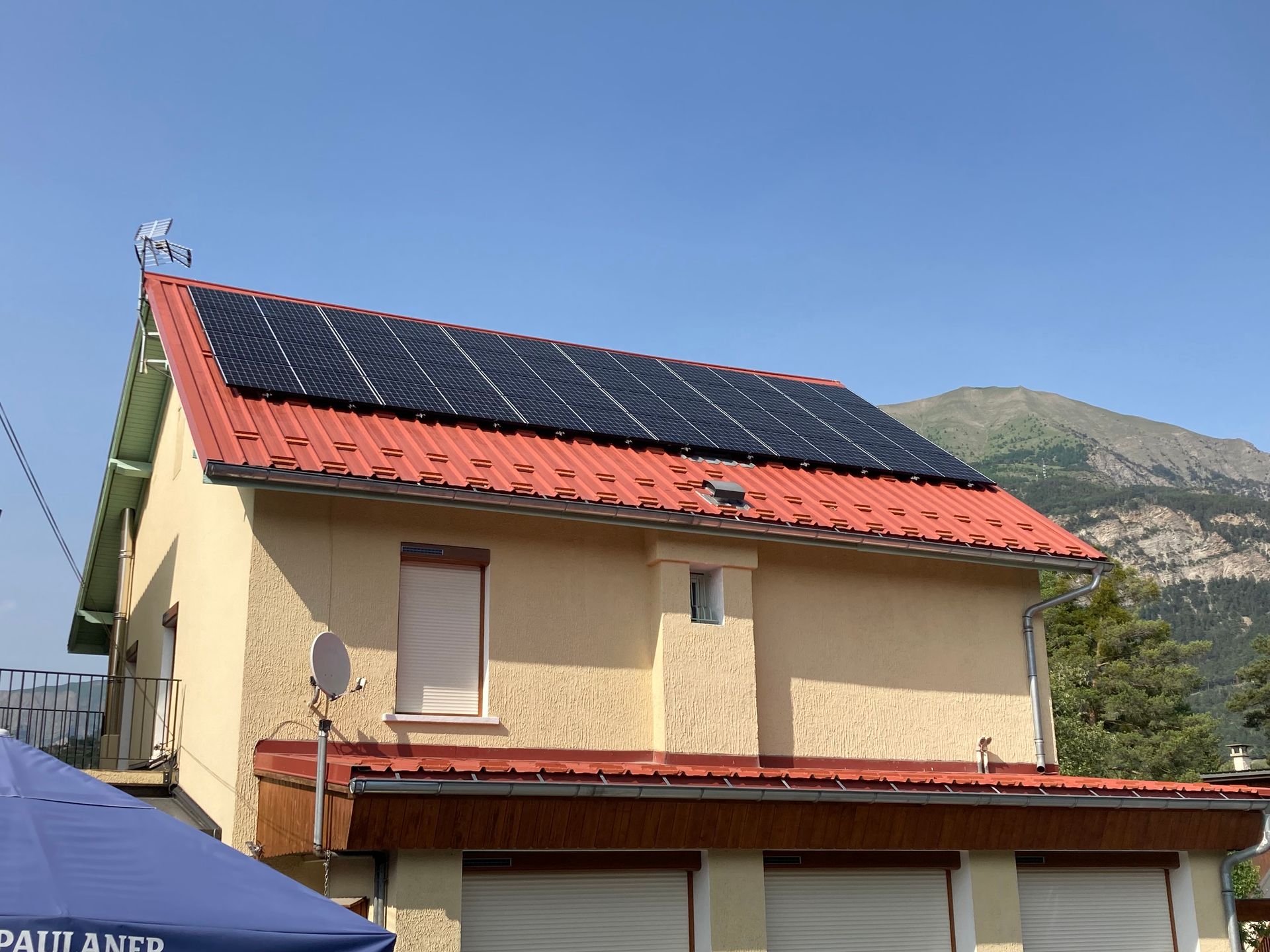 Une maison à la façade claire et au toit en tuile orange est équipée de rangées de panneaux photovoltaïques 